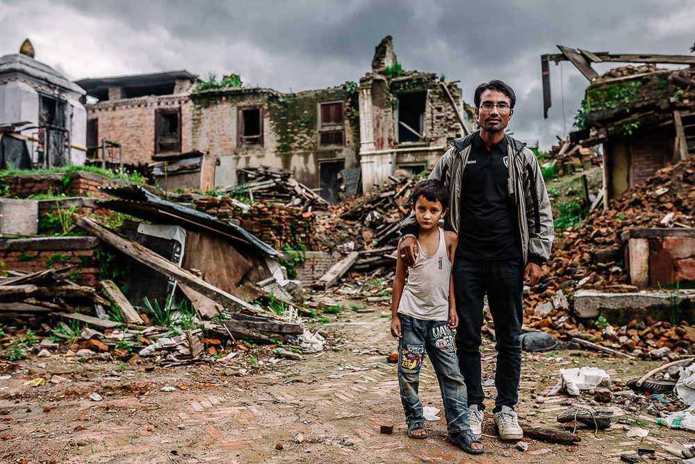 Man and son standing in front of demolished home, Nepal - Travel photojournalism