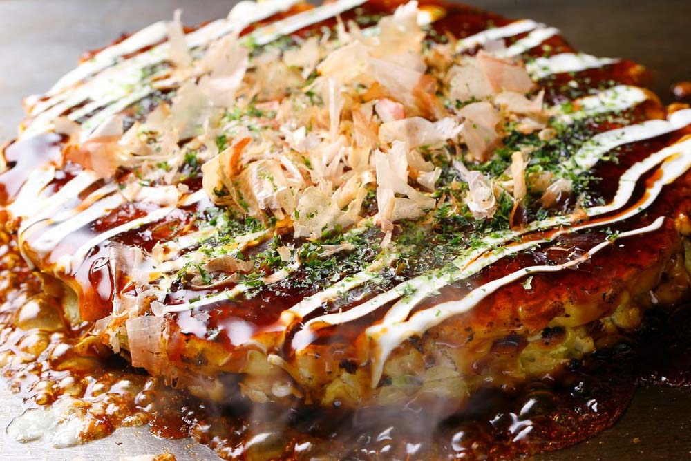 Okonomiyaki, a japanese style savoury pancake topped with bonito flakes and mayonaise - Osaka budget