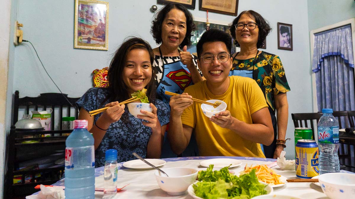 Four people smiling while eating traditional Vietnamese food in a Local's Home - Central Vietnam Itinerary