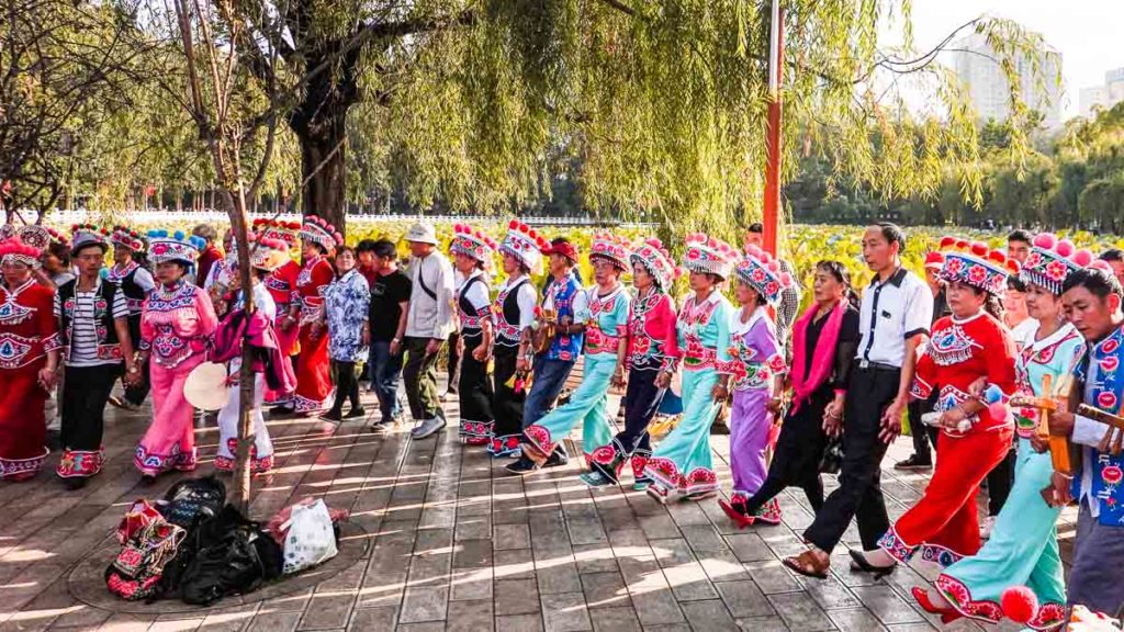 Locals in traditional ethnic costumes dancing at Cuihu green lake park China Things to do in Kunming city