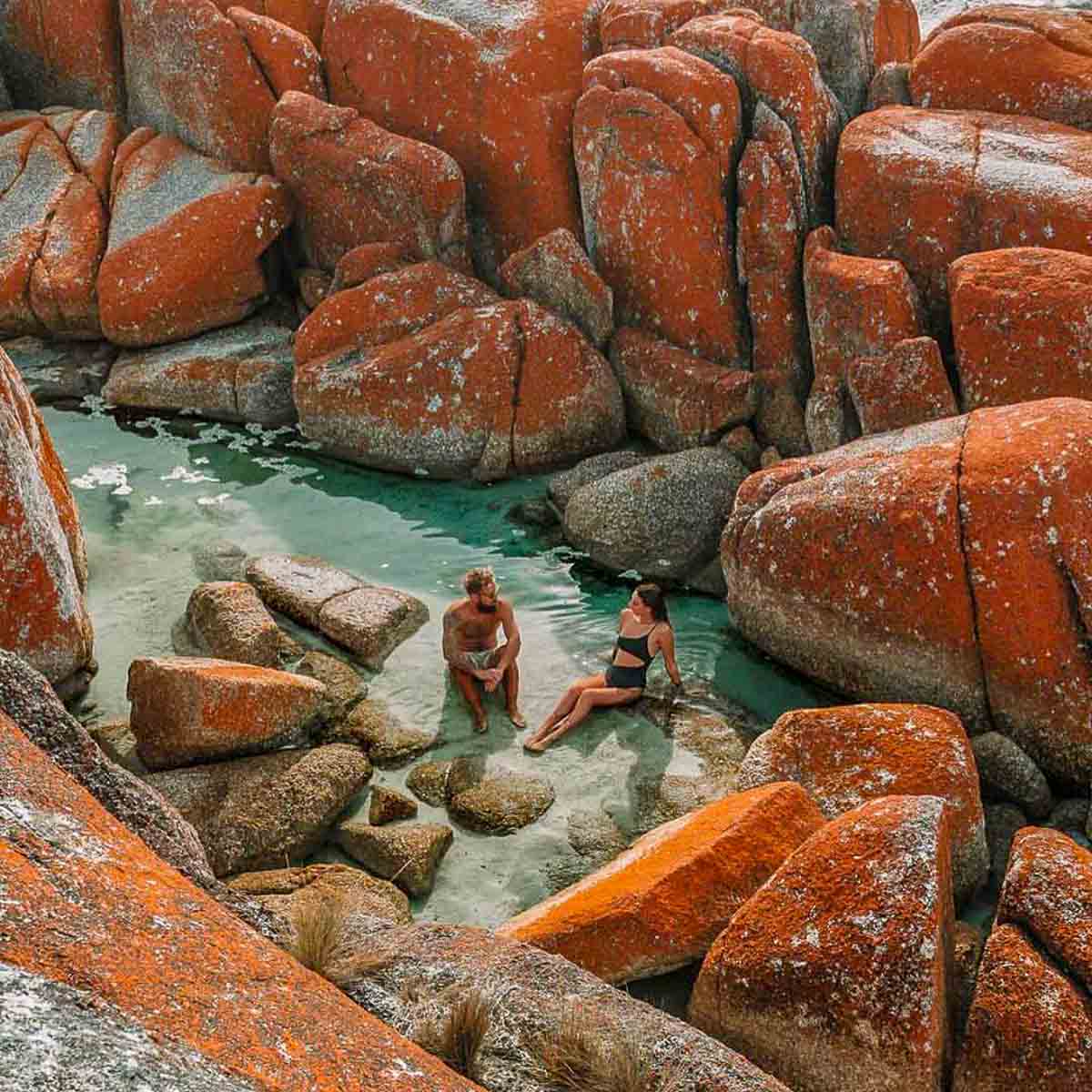 Couple relaxing at Bay of Fires - Places to visit in Tasmania