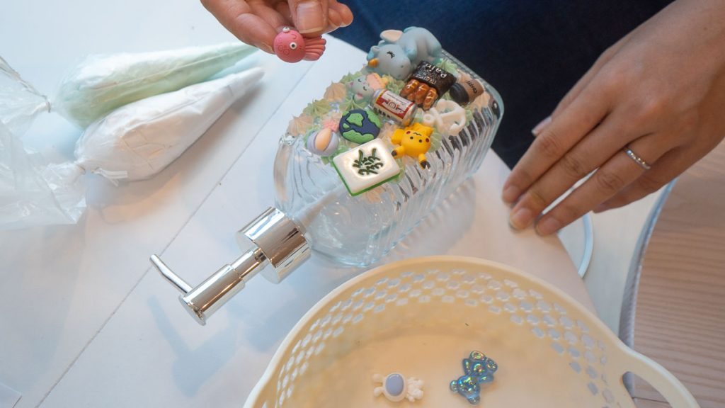 Person Putting Charms on Soap Bottle - JB Cafe