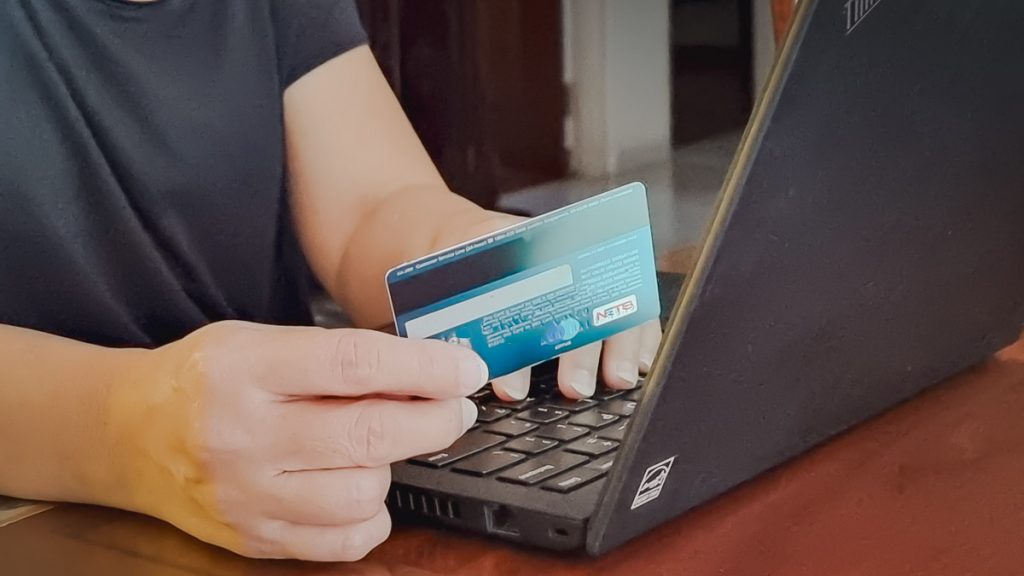 Person online shopping holding credit card in front of laptop - Travel budget hacks