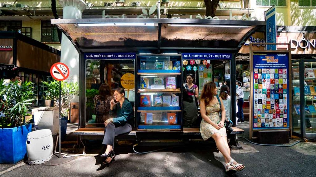 Two women sitting on a bus stop bench lined with books in Book Street - Things to do in Southern Vietnam