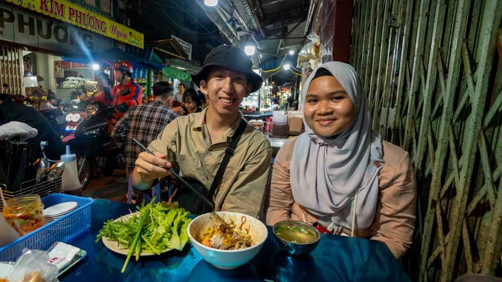two friends sitting in front of a bowl of noodles - ho chi minh nightlife