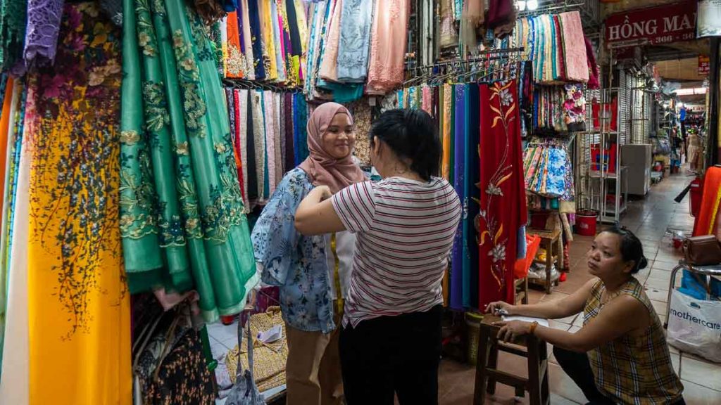 Girl in hijab getting measured by a Vietnamese seamstress in a fabric store at Ben Thanh Market - Things to do in Ho Chi Minh City