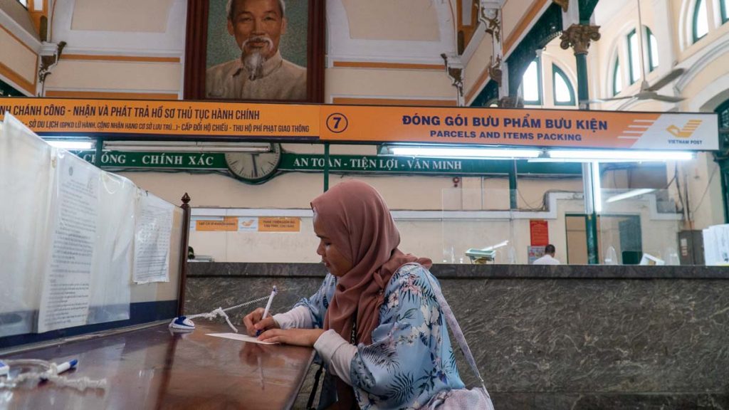 A girl writing a post card on a table in Sai Gon Central Post Office - Things to do in vietnam