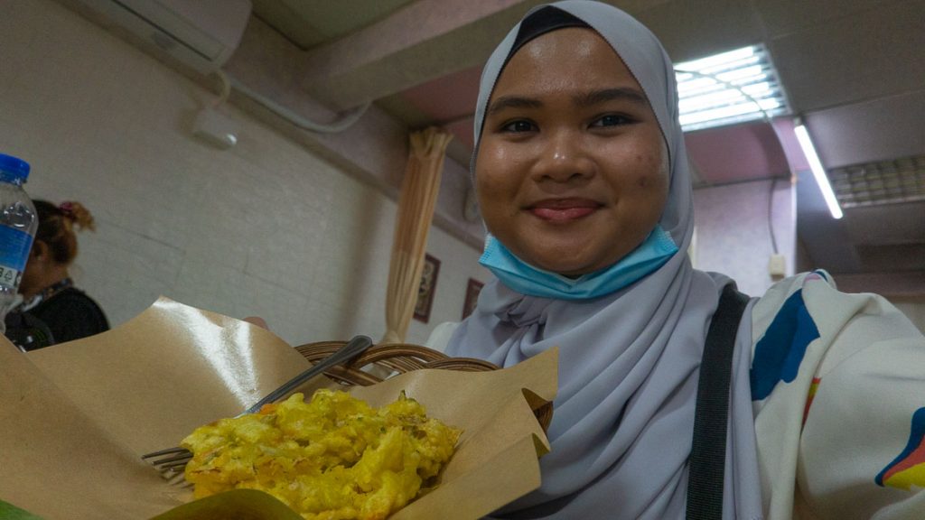 A girl in a hijab showing a bakwan vegetable fritter - Solo travel taiwan
