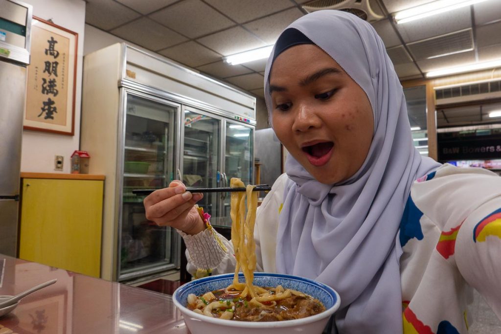 A girl in hijab holding up braised rib finger noodles from Halal Yellow Beef Noodle House - Solo travel taipei