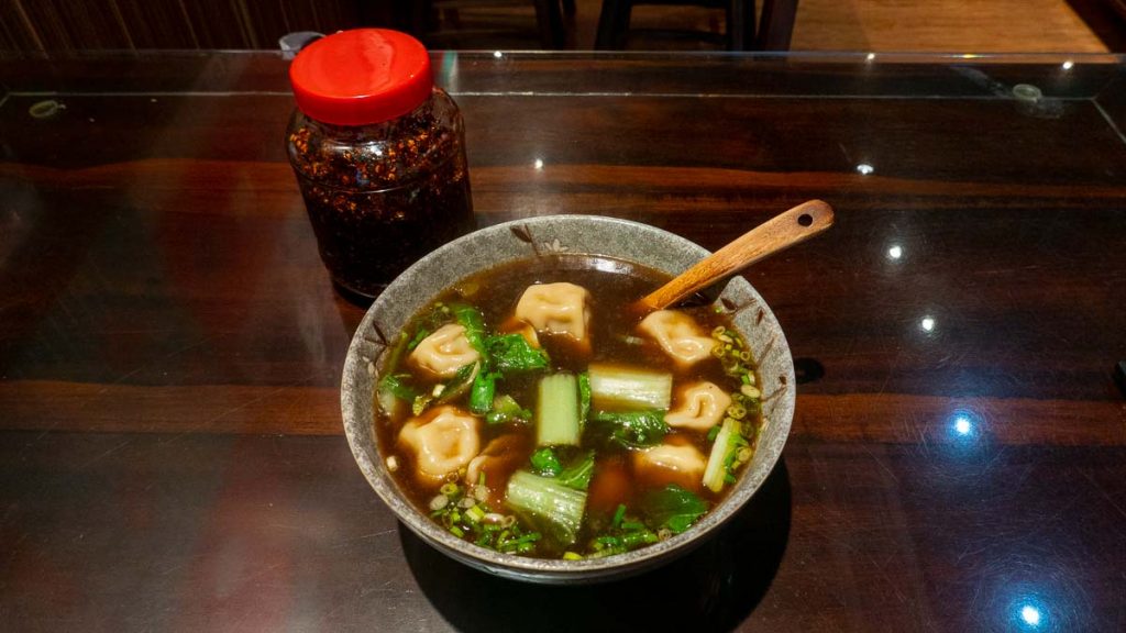 A bowl of dumplings in soup and a jar of chili oil - Halal food in Taipei