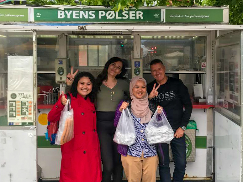 four people posing and smiling in front of a danish hot dog cart byens pølser - Denmark Nørrebro