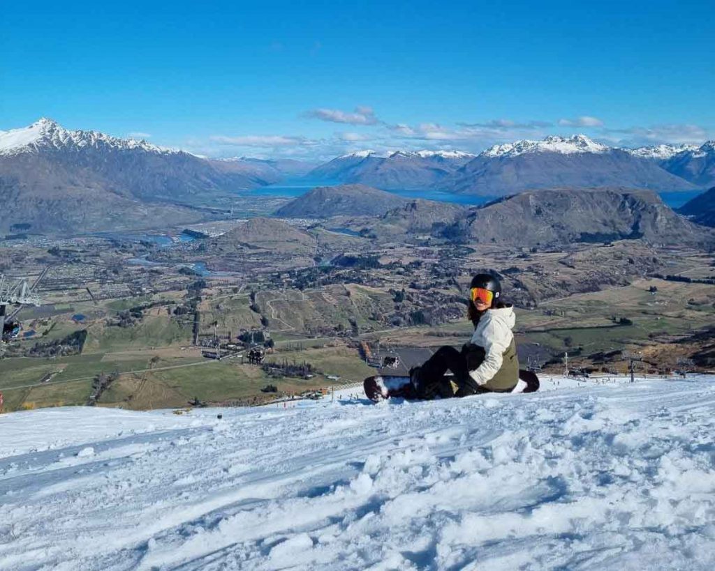 Woman sitting on the alps while snowboarding in Queenstown - New Zealand Off-Peak