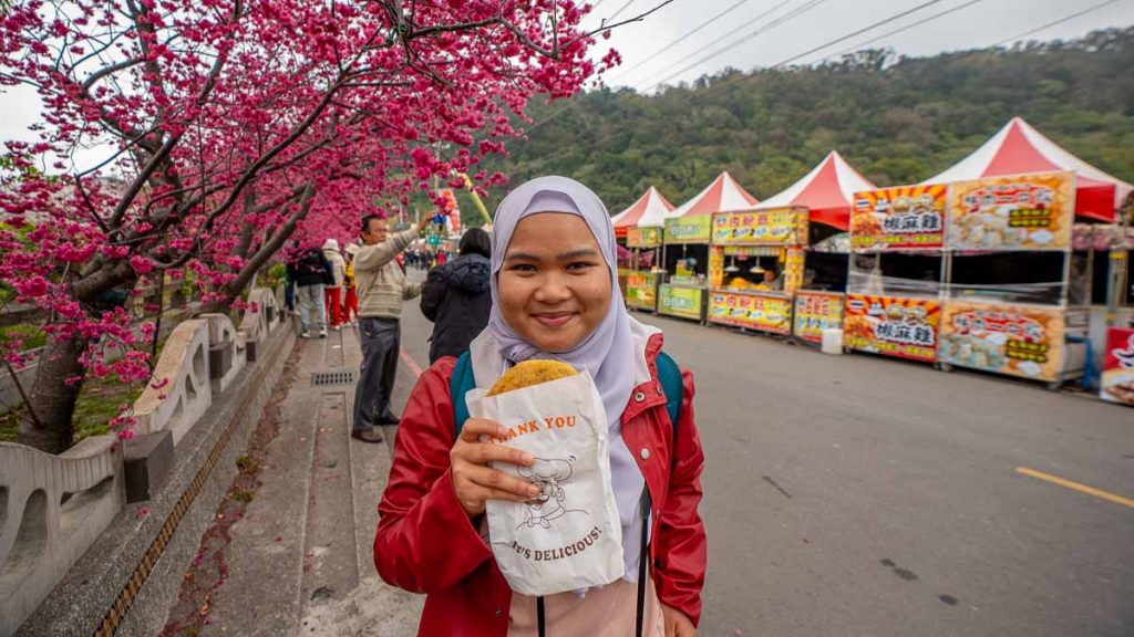 girl holding a spring onion shao bing near the cherry blossoms at tai'an police station - things to do in taiwan