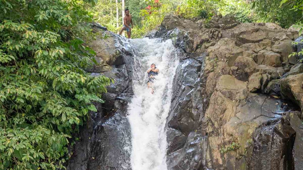 Man sliding off Kroya Waterfall Natural Waterslide - Bali Itinerary