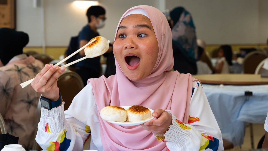 a girl in a hijab enjoying a pan fried chicken bun and halal dim sum - Halal dining experiences in Hong Kong