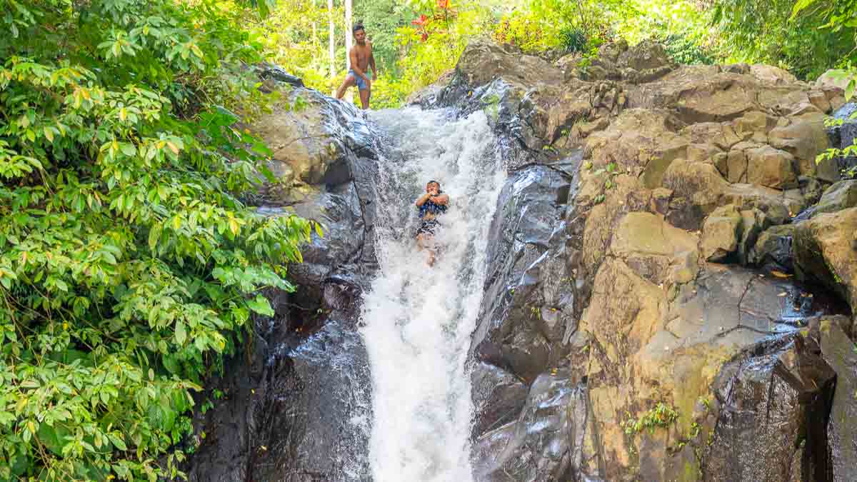 Man sliding off Kroya Waterfall Natural Waterslide - Bali Itinerary