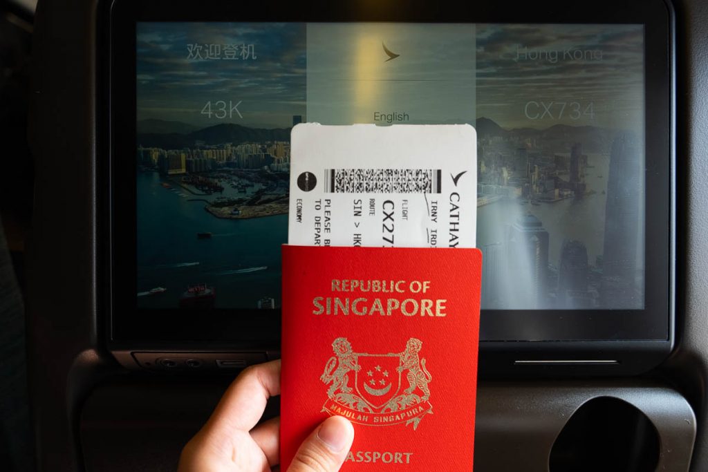 a singaporean passport in front of cathay pacific's in-flight entertinement - hong kong itinerary