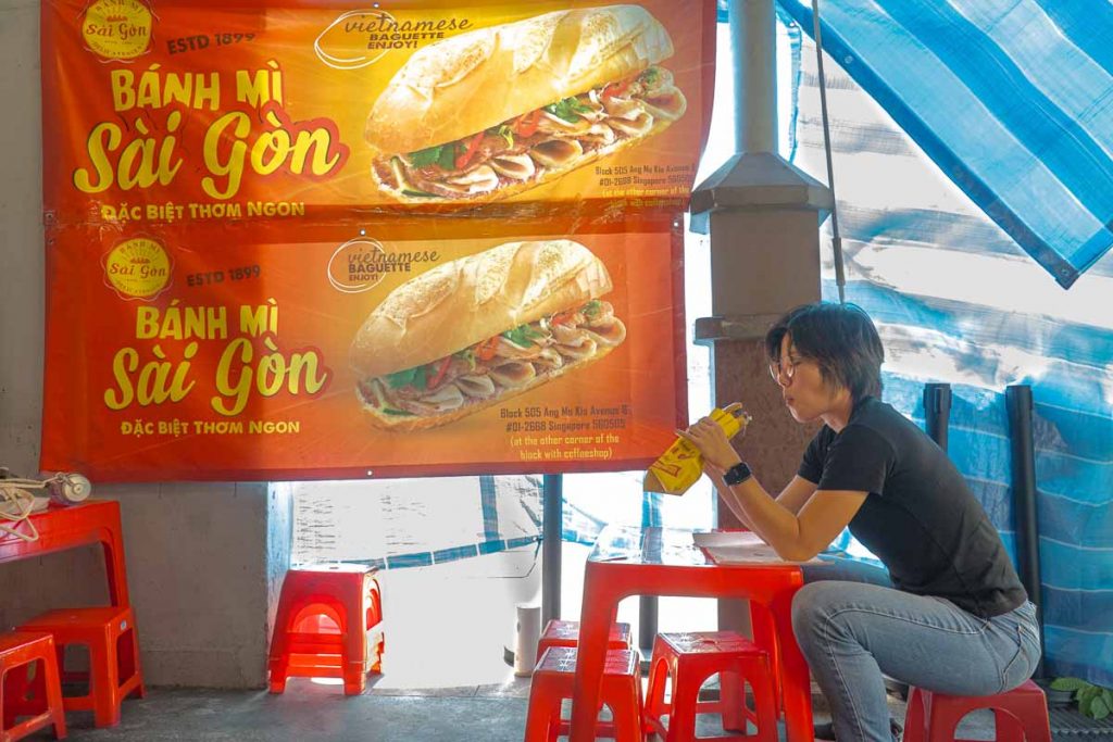 Woman eating sandwich at Banh Mi Saigon seats - Things To Do In Ang Mo Kio