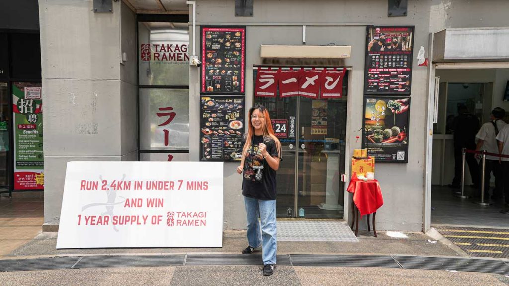Girl in front of Ramen Shop, with sign stating running challenge - Things To Do In Ang Mo Kio