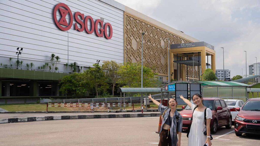 Two people pointing to Mid Valley Shopping Mall behind them