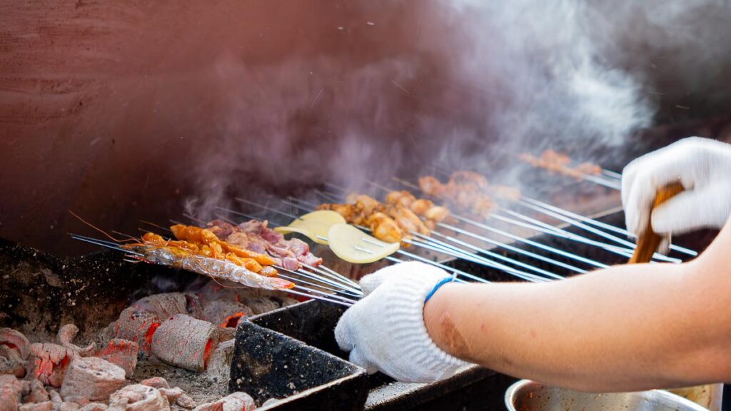 Person grilling chinese skewers, aka chuan chuan, on a charcoal grill at Lai Lai BBQ Mount Austin