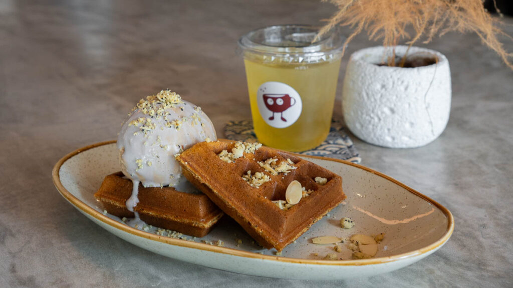 Close-up of Podd's Favourite: Earl Grey waffles with Earl Grey ice cream, topped with lavender sauce and Earl Grey crumble. Behind it lies an Iced Kukicha