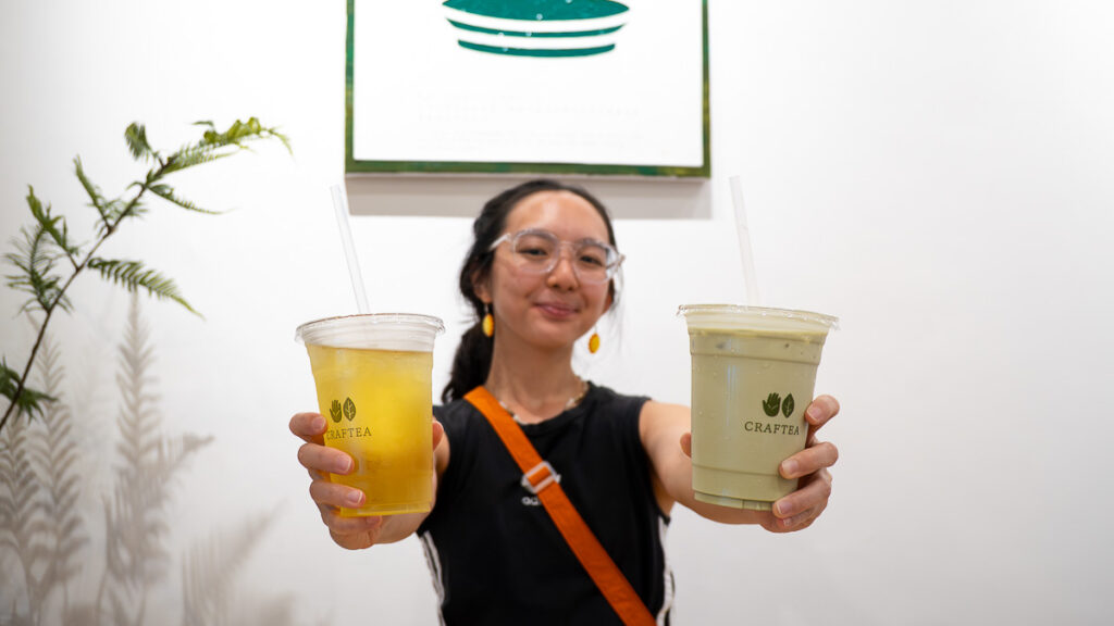 Person holding up two drinks at Craftea, Sencha Kyoto Tea and RIch Genmaicha Latte