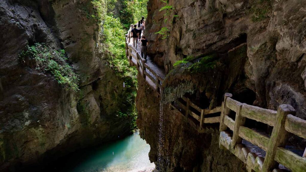 Top-down view of Longshuixia Fissure Gorge trail wrapping around a side of the canyon, with a teal stream of water below.