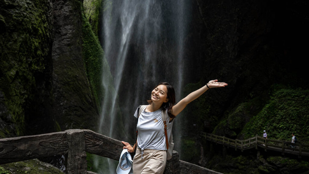 Person posing happily in front of the Galaxy Waterfall, Longshuixia Fissure Gorge