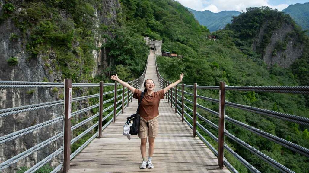 Person posing happily on the Sky Gate Suspension Bridge, Wuling Mountain Great Rift Valley