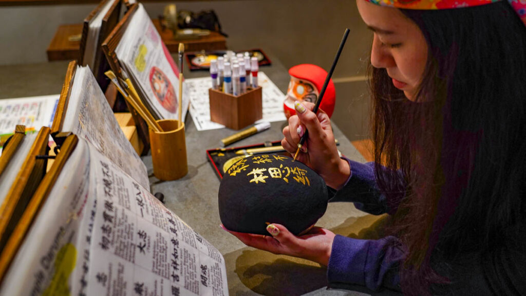 Girl painting Daruma - Lesser-known things to do in Osaka